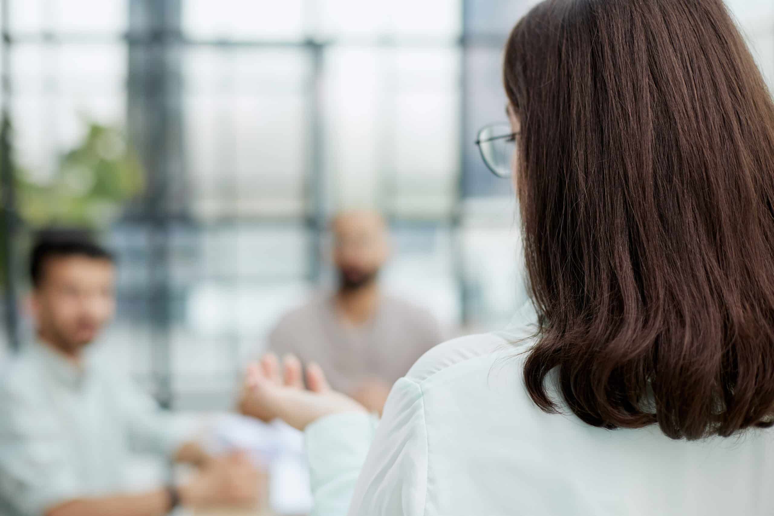 Rear view female participant sharing personal problem with colleagues or corporate staff